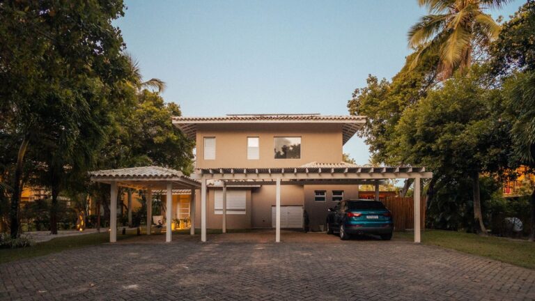 Materialwahl für Überdachungen und Bauten: Eigenschaften und Einsatzgebiete von Kunststoffplatten Exterior view of a modern house with a driveway and palm trees at sunset, offering a serene tropical ambiance.